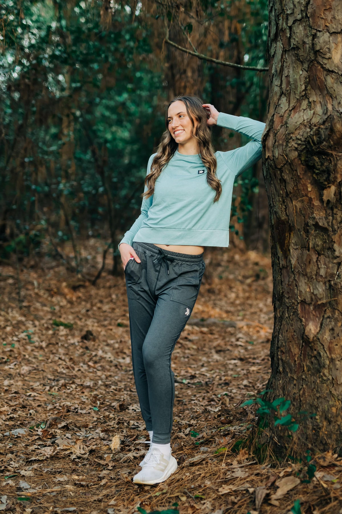 MOVE sport apparel woman wearing a light blue long sleeve crewneck sweatshirt and dark grey joggers in a forest.