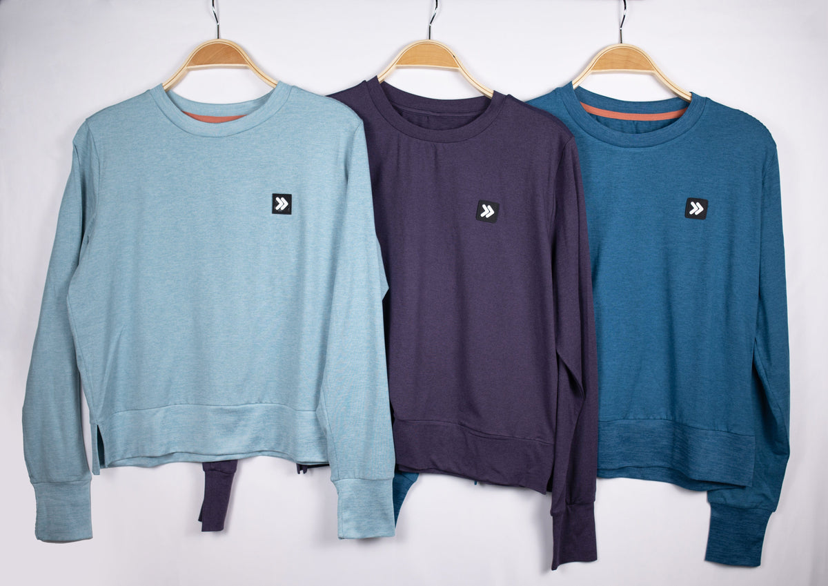 MOVE sport apparel Black Label crewneck sweatshirts in light blue, dark purple, and teal hanging on wooden hangers.