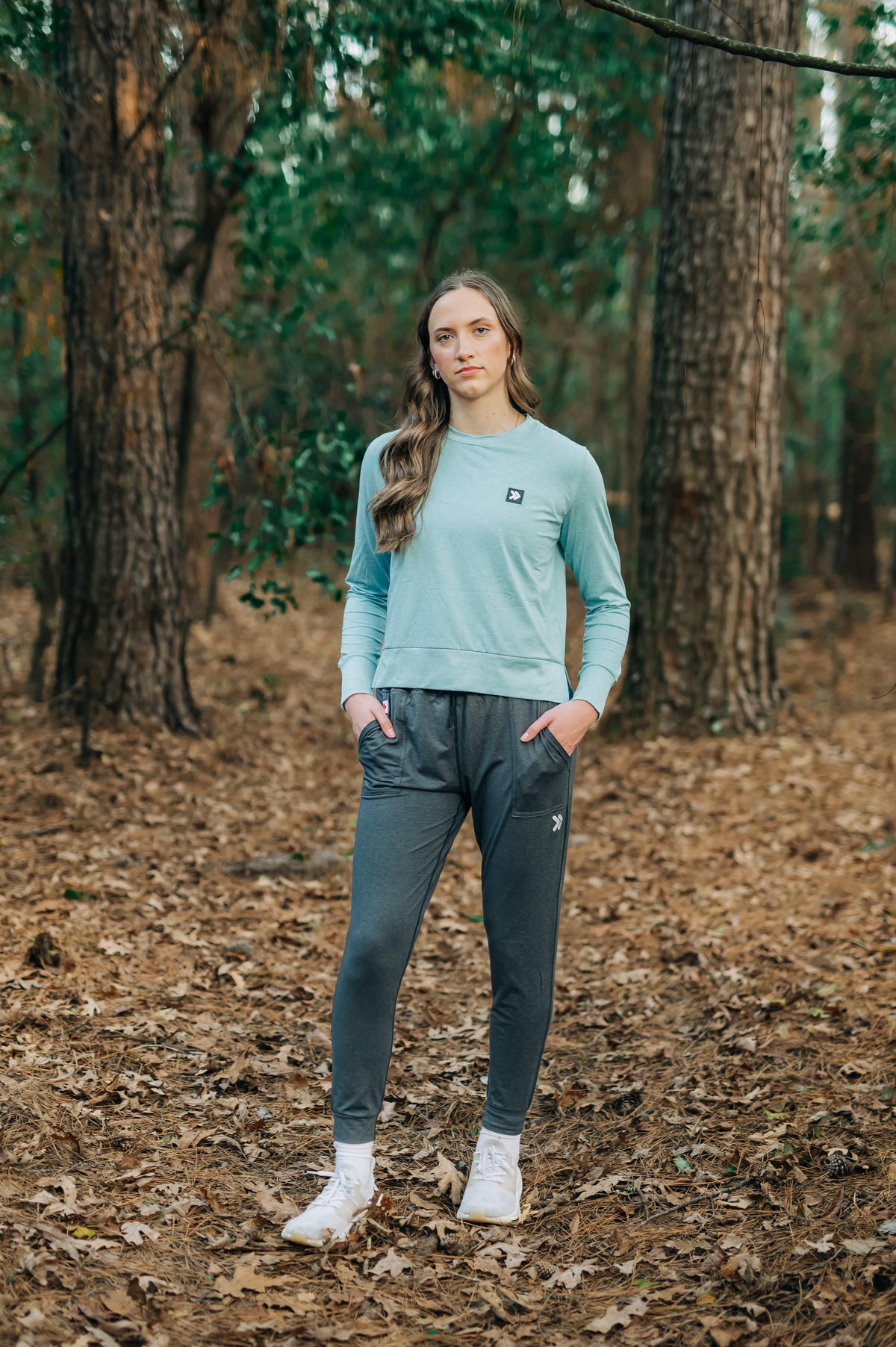 MOVE sport apparel model wearing a light blue long sleeve crewneck sweatshirt and dark grey joggers in a forest.