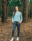 MOVE sport apparel model wearing a light blue long sleeve crewneck sweatshirt and dark grey joggers in a forest.
