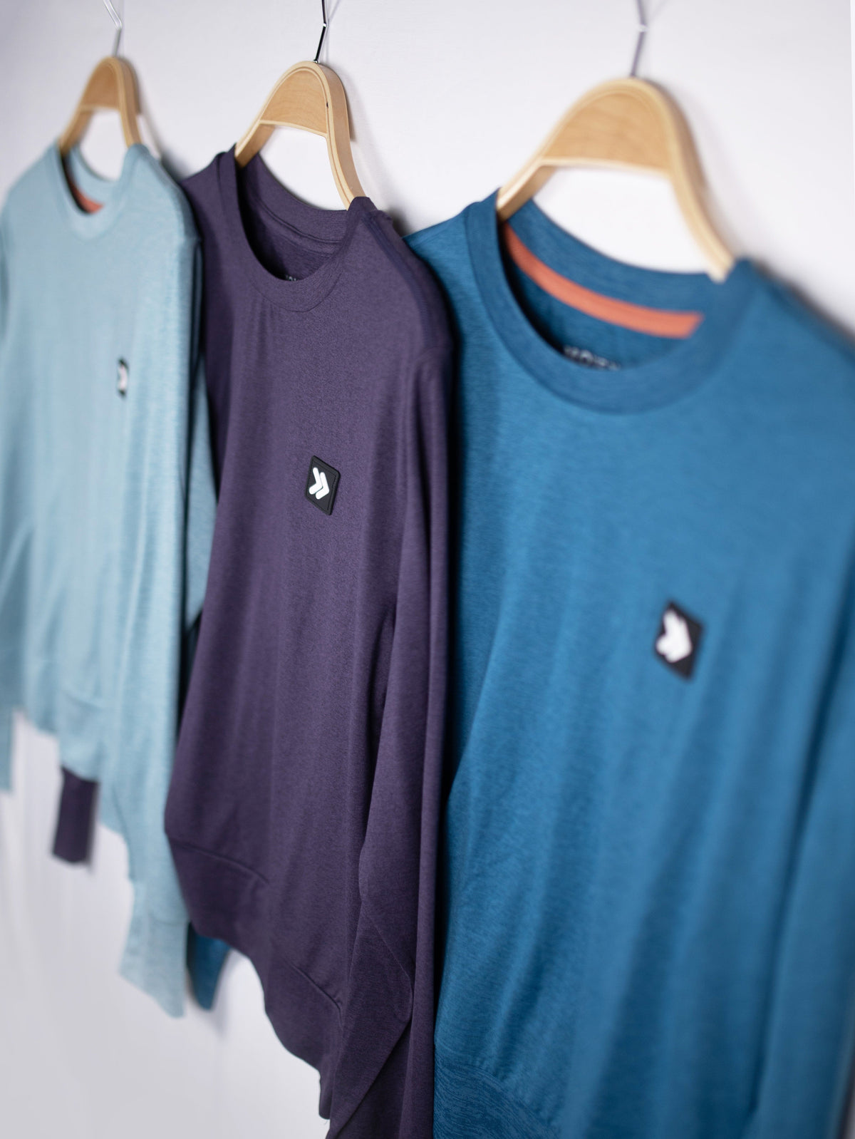 MOVE sport apparel crewneck sweatshirts in light blue, dark purple, and teal hanging on wooden hangers