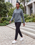 Female model walking through a modern urban park wearing MOVE Sport Apparel women’s Balsam Green waffle hoodie, black training pants and white athletic sneakers.