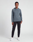 Full-body female studio model wearing MOVE Sport Apparel women’s Balsam Green waffle hoodie with black training pants and white sneakers.