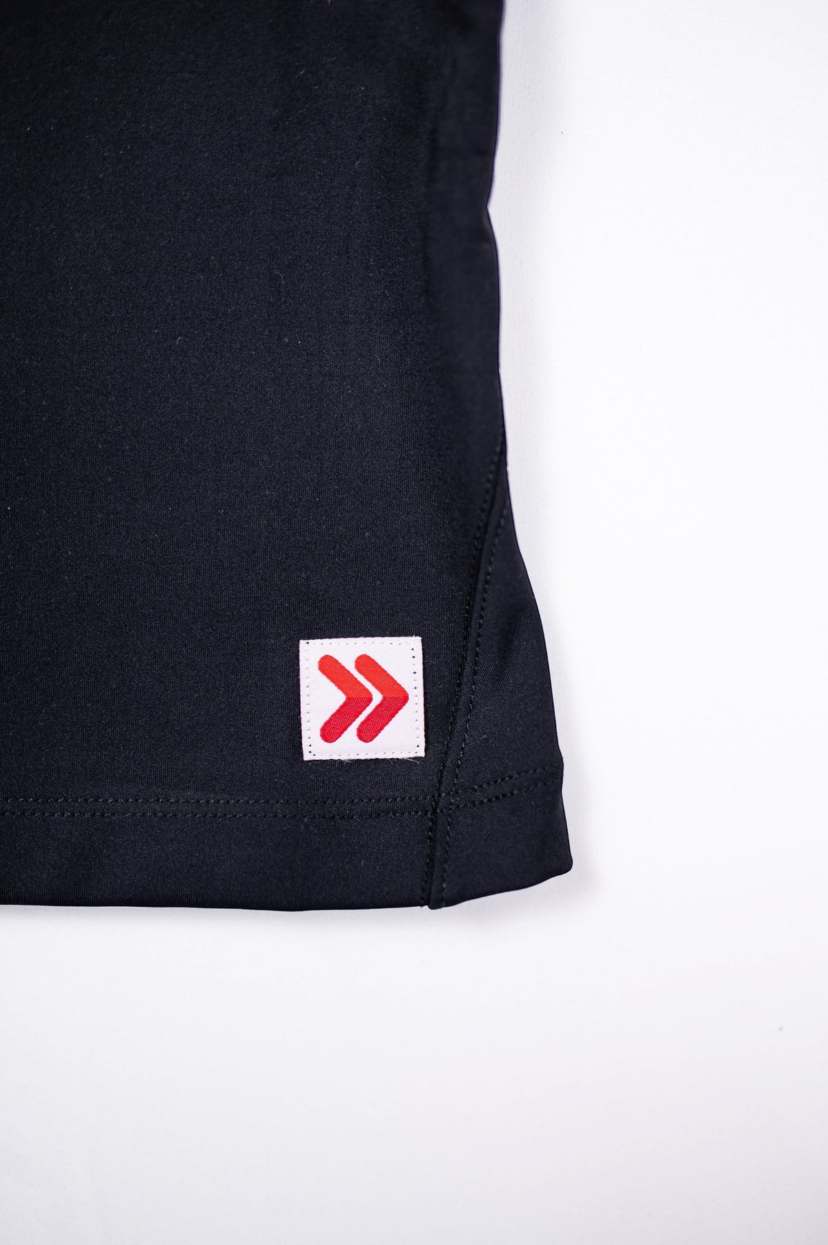 Close view of the original red double-chevron hem tab on the Black MOVE Sport Apparel Pure Stretch Full Length Tank Top.