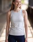 Woman wearing MOVE Sport Apparel Pure Stretch Full Length Tank Top in White beside a sunlit walkway.