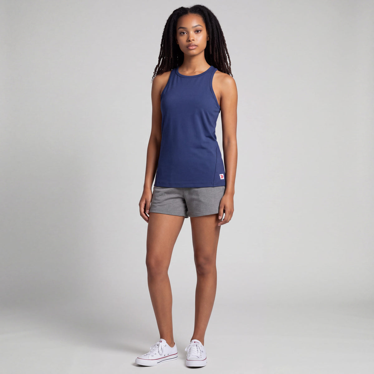 Full-body studio view of a woman wearing MOVE Sport Apparel Pure Stretch Full Length Tank Top in Maritime Blue with grey shorts and white trainers.