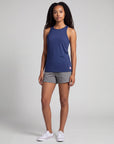 Full-body studio view of a woman wearing MOVE Sport Apparel Pure Stretch Full Length Tank Top in Maritime Blue with grey shorts and white trainers.