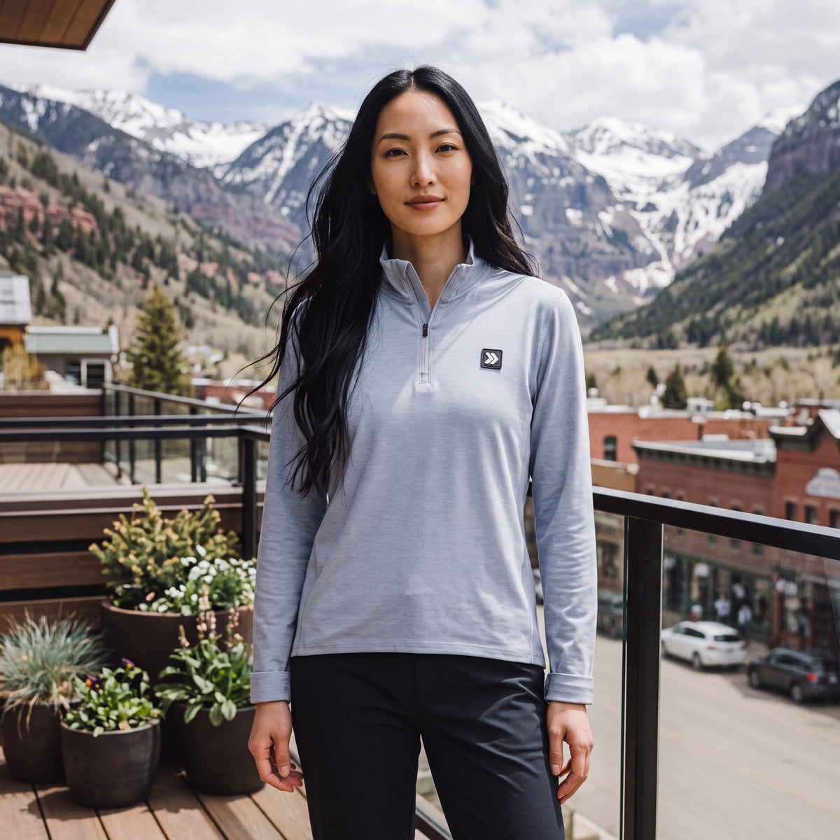 Woman wearing the MOVE Sport Apparel Women’s Essential Quarter Zip in Silver Cloud on a balcony overlooking mountains.
