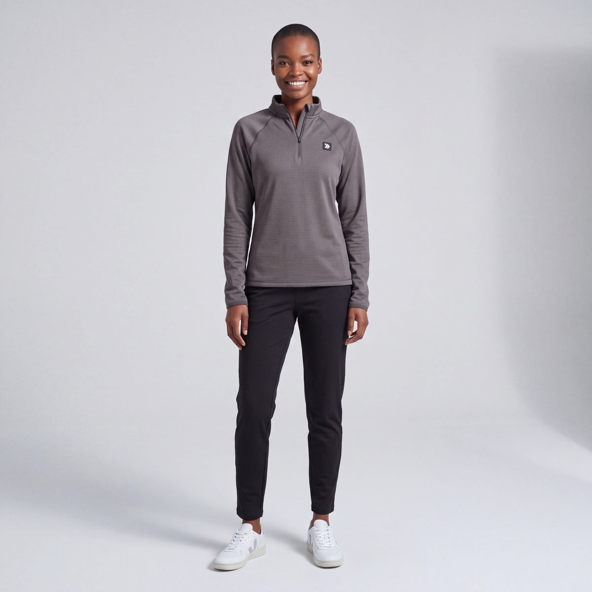 Full-body female model wearing the charcoal MOVE Sport Apparel women’s waffle quarter zip with black athletic pants in a neutral studio.