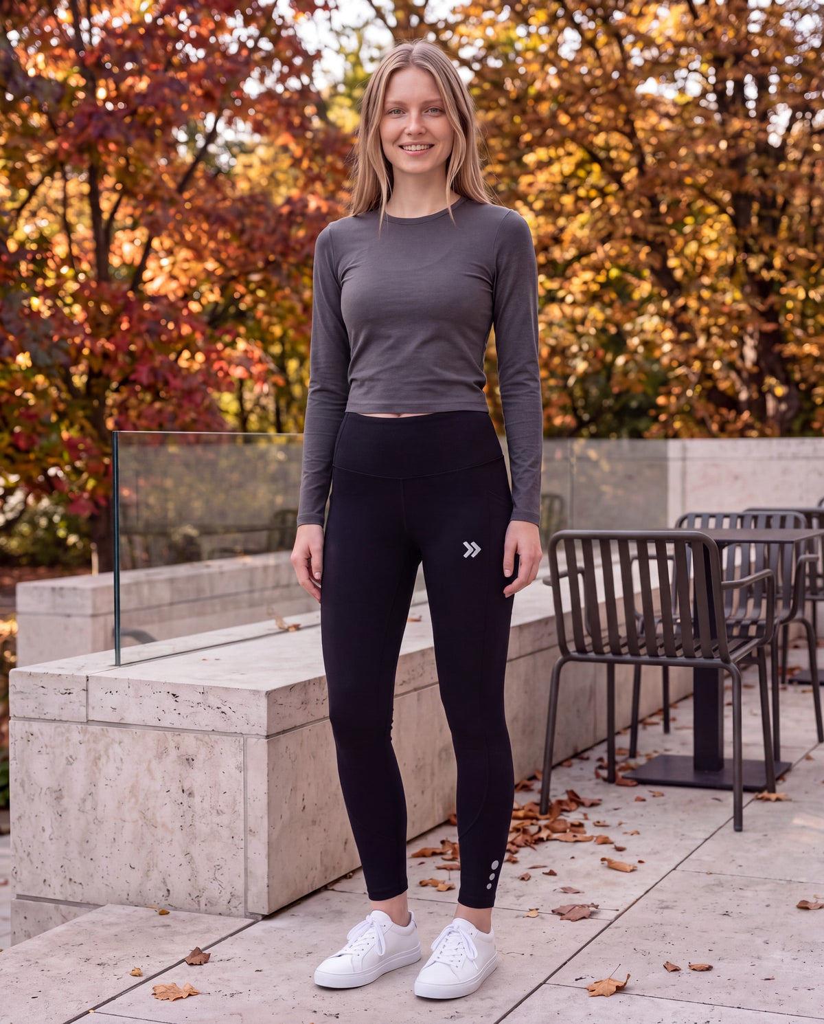 Woman wearing black MOVE Sport Apparel Women’s Brushed Running Leggings with a charcoal long-sleeve top on a stone terrace beside autumn trees.