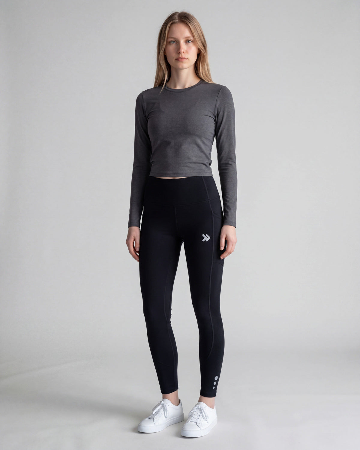 Woman modeling black MOVE Sport Apparel Women’s Brushed Running Leggings with a charcoal long-sleeve top and white shoes in a neutral studio.