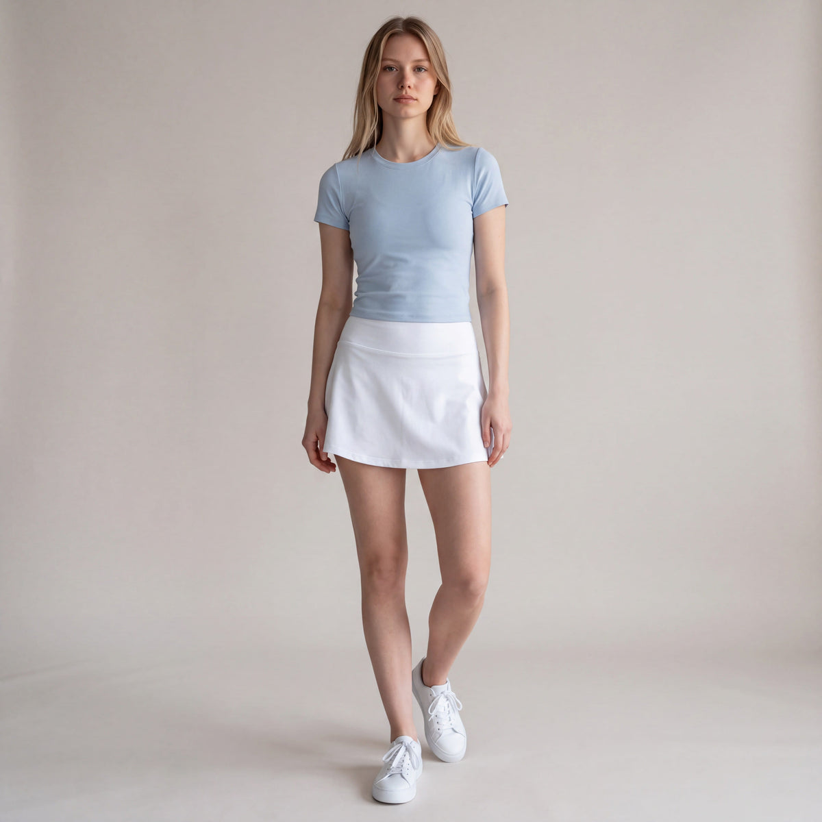 MOVE Sport Apparel Women’s Active Skort in White, front view worn by an adult woman in a neutral studio with a pale blue athletic top and white court shoes.