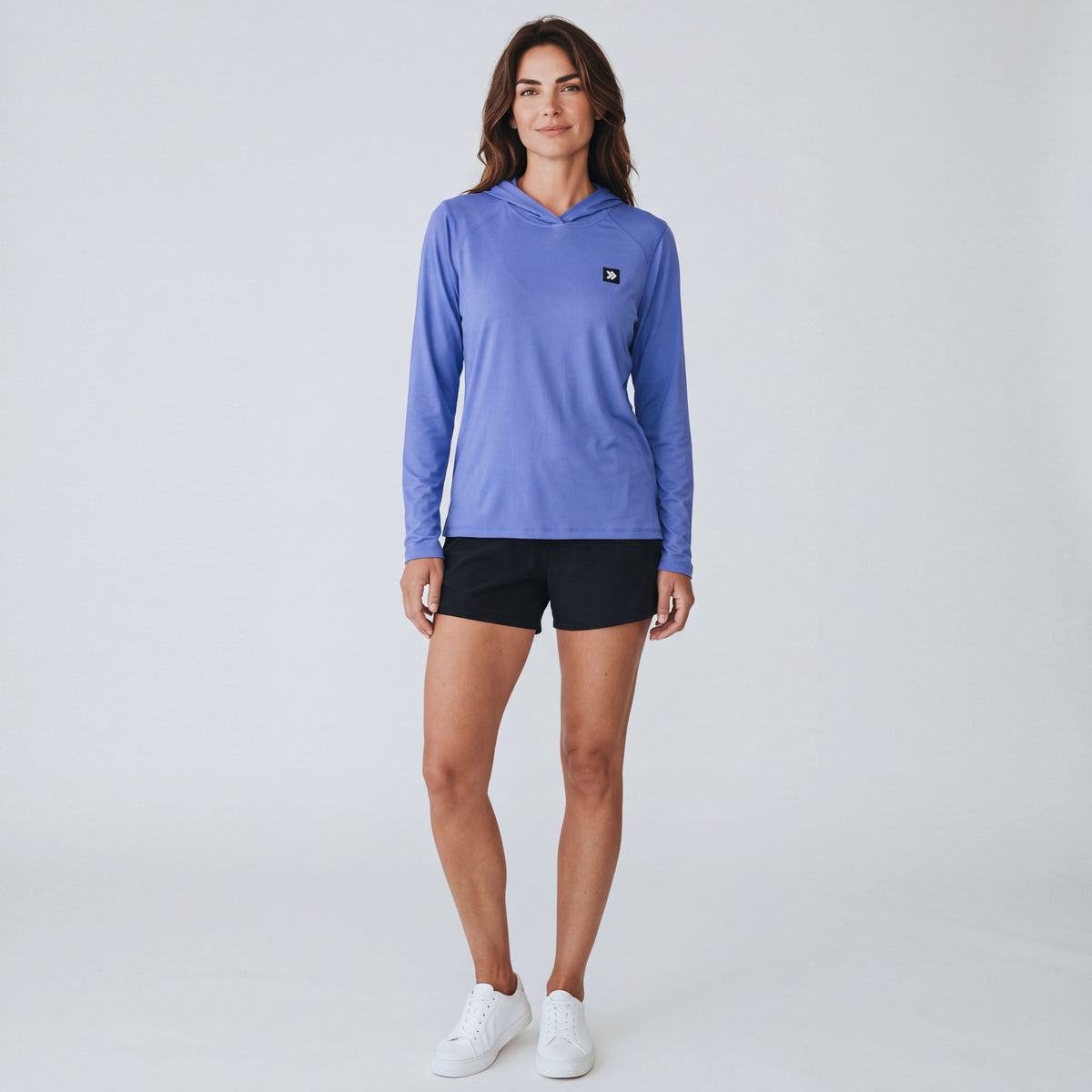 Full-body studio view of a woman wearing MOVE Sport Apparel women’s Black Label Lightweight Sun Hoodie in Deep Periwinkle with black shorts and white trainers.