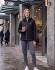 Woman wearing the black MOVE Sport Apparel waterproof jacket outside a café after rain, holding a coffee.