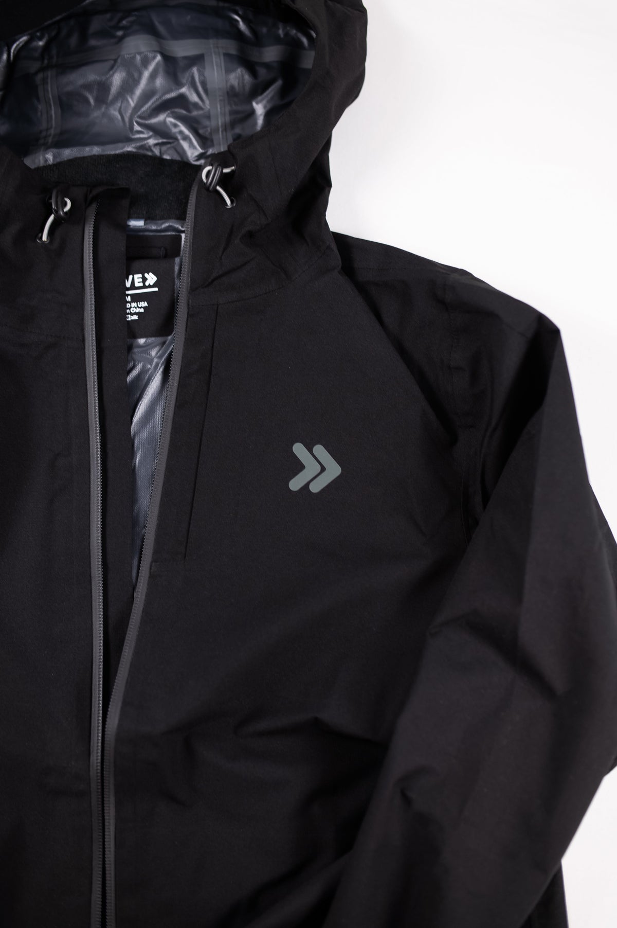 Black MOVE Sport Apparel women’s waterproof jacket showing the hood, zipper and original small gray chest embellishment.