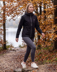Woman stepping onto a low stone on an autumn woodland trail in the black MOVE Sport Apparel waterproof jacket.