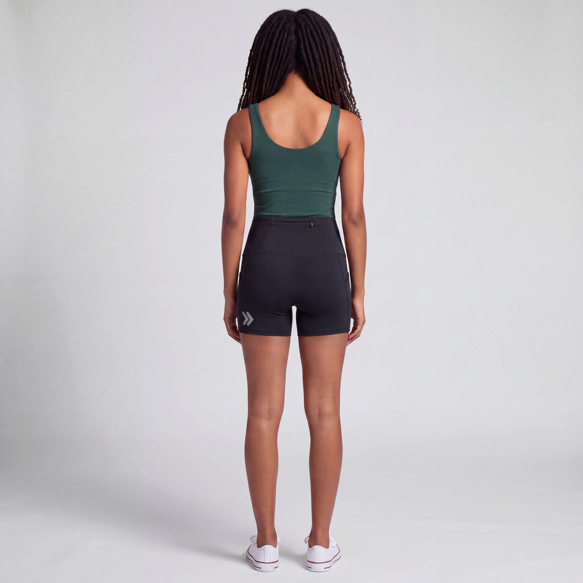 Rear studio view of a woman wearing black MOVE Sport Apparel Women’s Biker Shorts, showing the short inseam, rear waistband zipper and silver embellishment near the back hem.