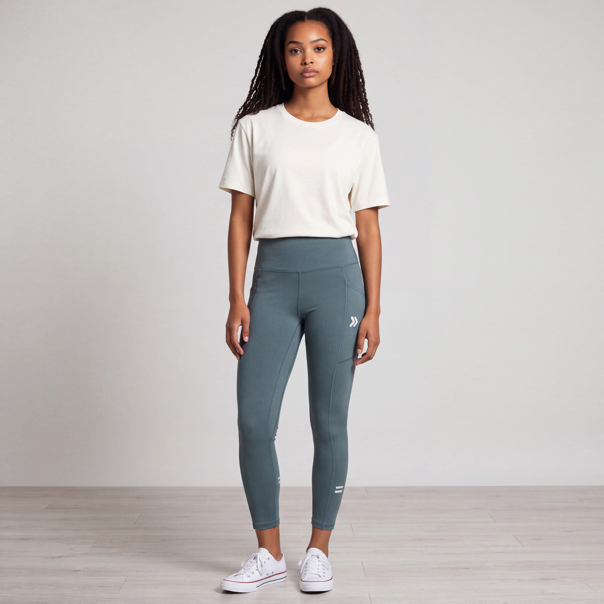 Full-body studio view of a woman wearing MOVE Sport Apparel women’s 25-Inch Running Tights in Balsam Green with an ivory top and white trainers.