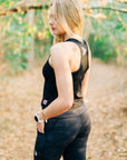 Rear three-quarter woodland view of a woman wearing MOVE Sport Apparel women’s 25-Inch Running Tights in Black Camouflage.