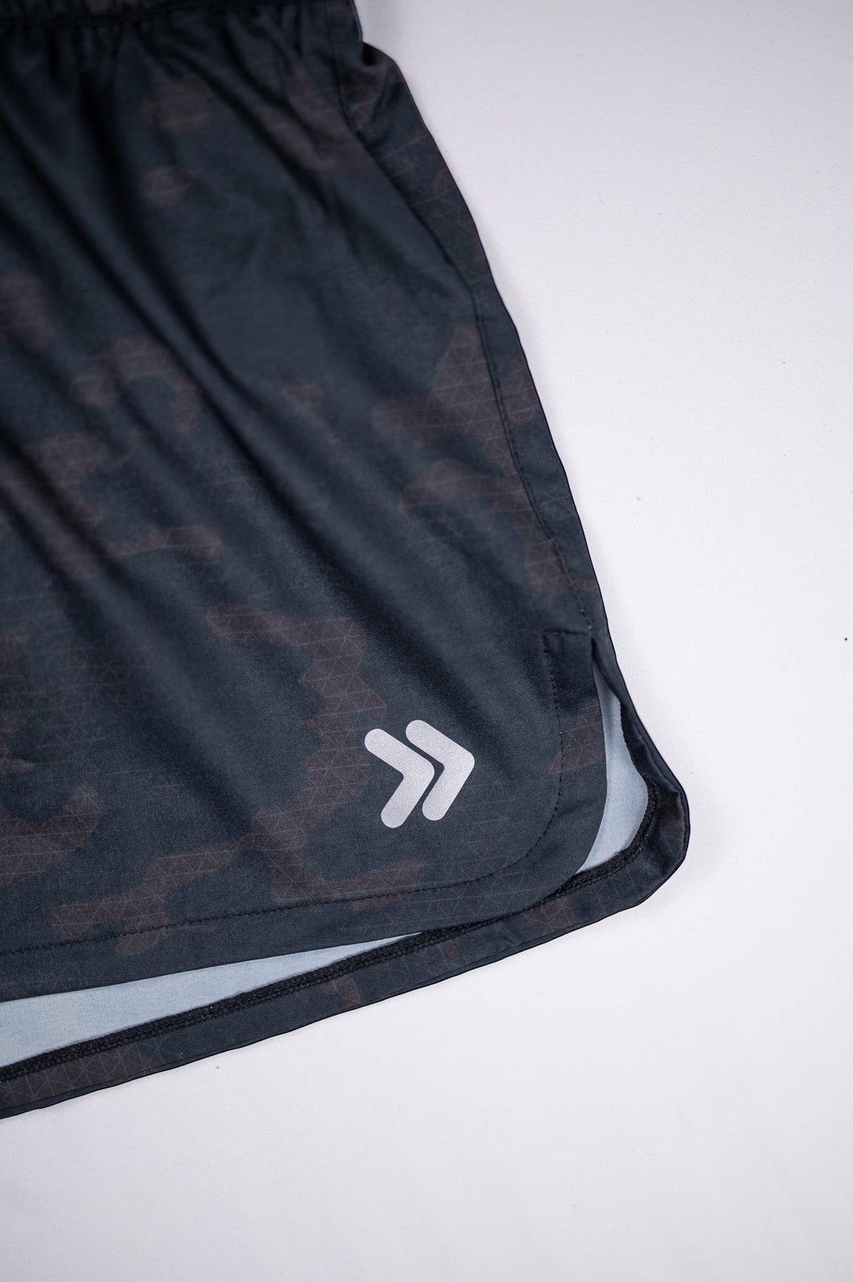 Close-up of the original white double-chevron embellishment on black camouflage running shorts.