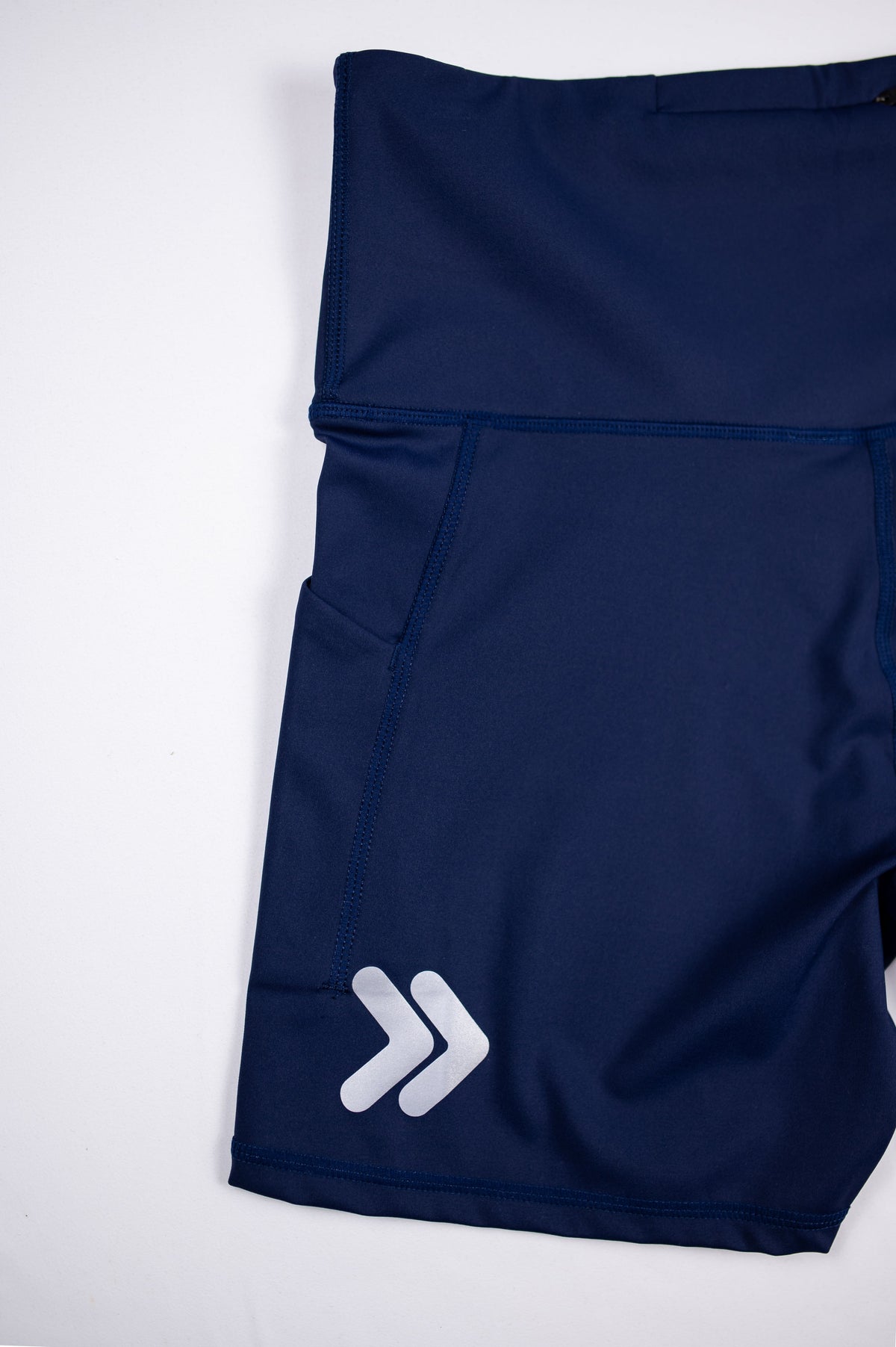 Close view of the original silver double-chevron embellishment near the hem of Maritime Blue MOVE Sport Apparel Women’s Biker Shorts.