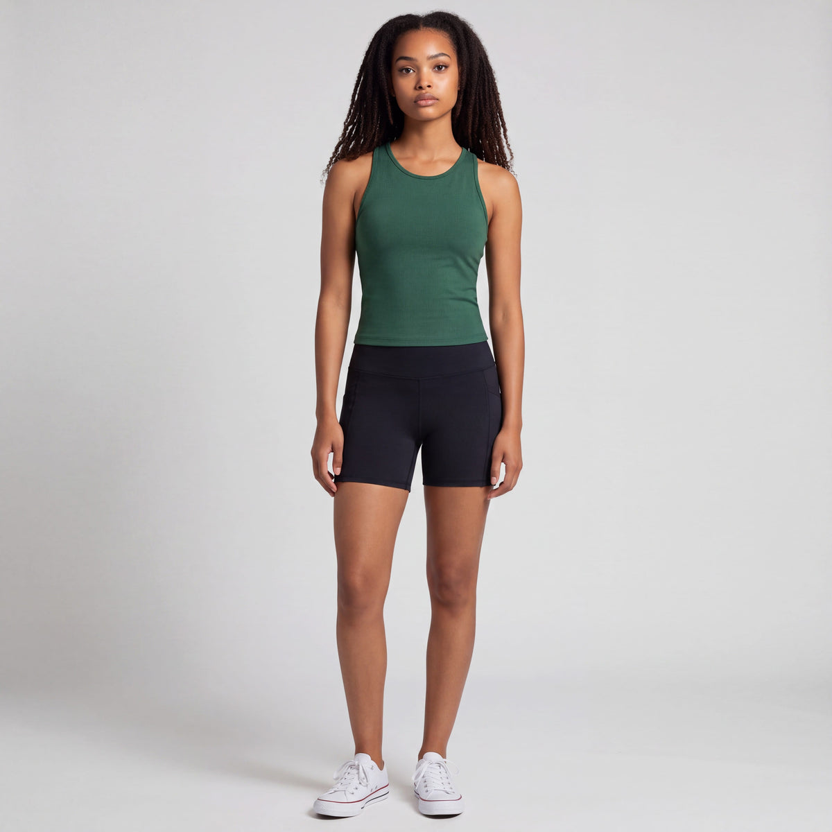 Front studio view of a woman wearing black MOVE Sport Apparel Women’s Biker Shorts with a short inseam, forest-green tank and white trainers.