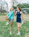 MOVE Sport Apparel women’s Black Label Lightweight Sun Hoodie: Woman wearing Aqua Splash sun hoodie during a standing quadriceps stretch on grass.