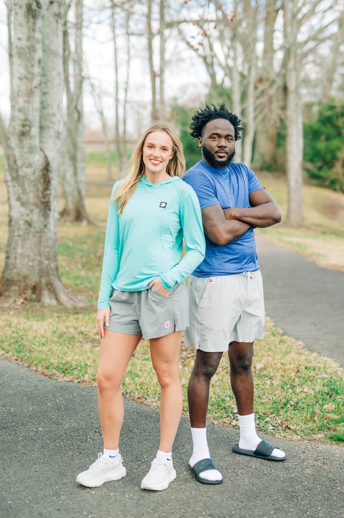 MOVE Sport Apparel women’s Black Label Lightweight Sun Hoodie: Woman wearing Aqua Splash sun hoodie and grey shorts beside a man on a woodland path.