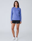 Full-body studio view of a woman wearing MOVE Sport Apparel women’s Black Label Lightweight Sun Hoodie in Deep Periwinkle with black shorts and white trainers.