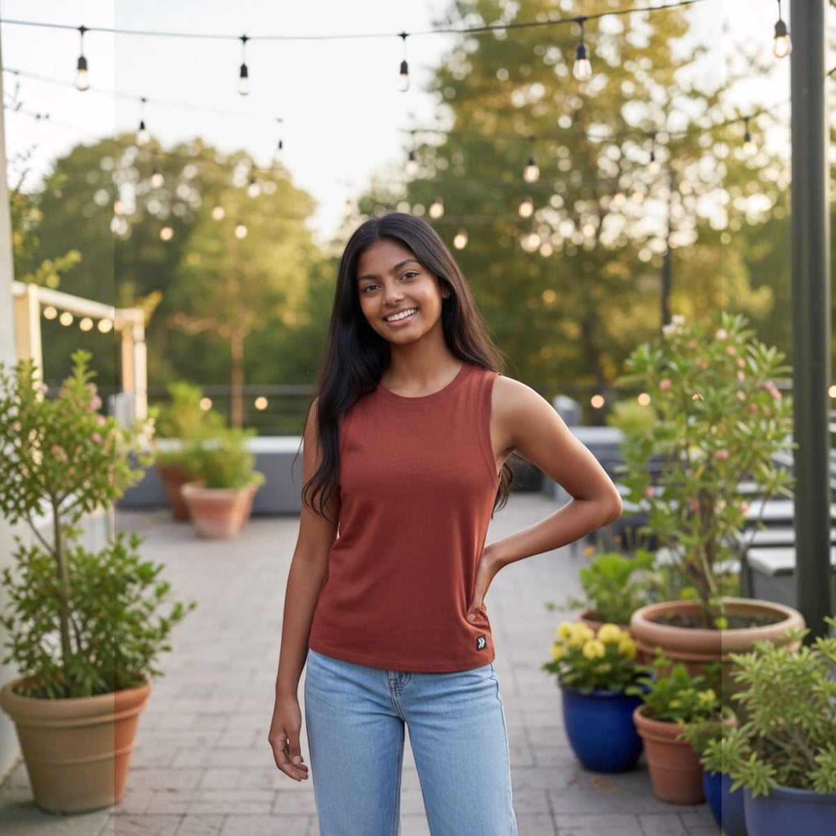 Woman wearing an oxblood red Essential High Neck Tank Top on a plant-lined patio.
