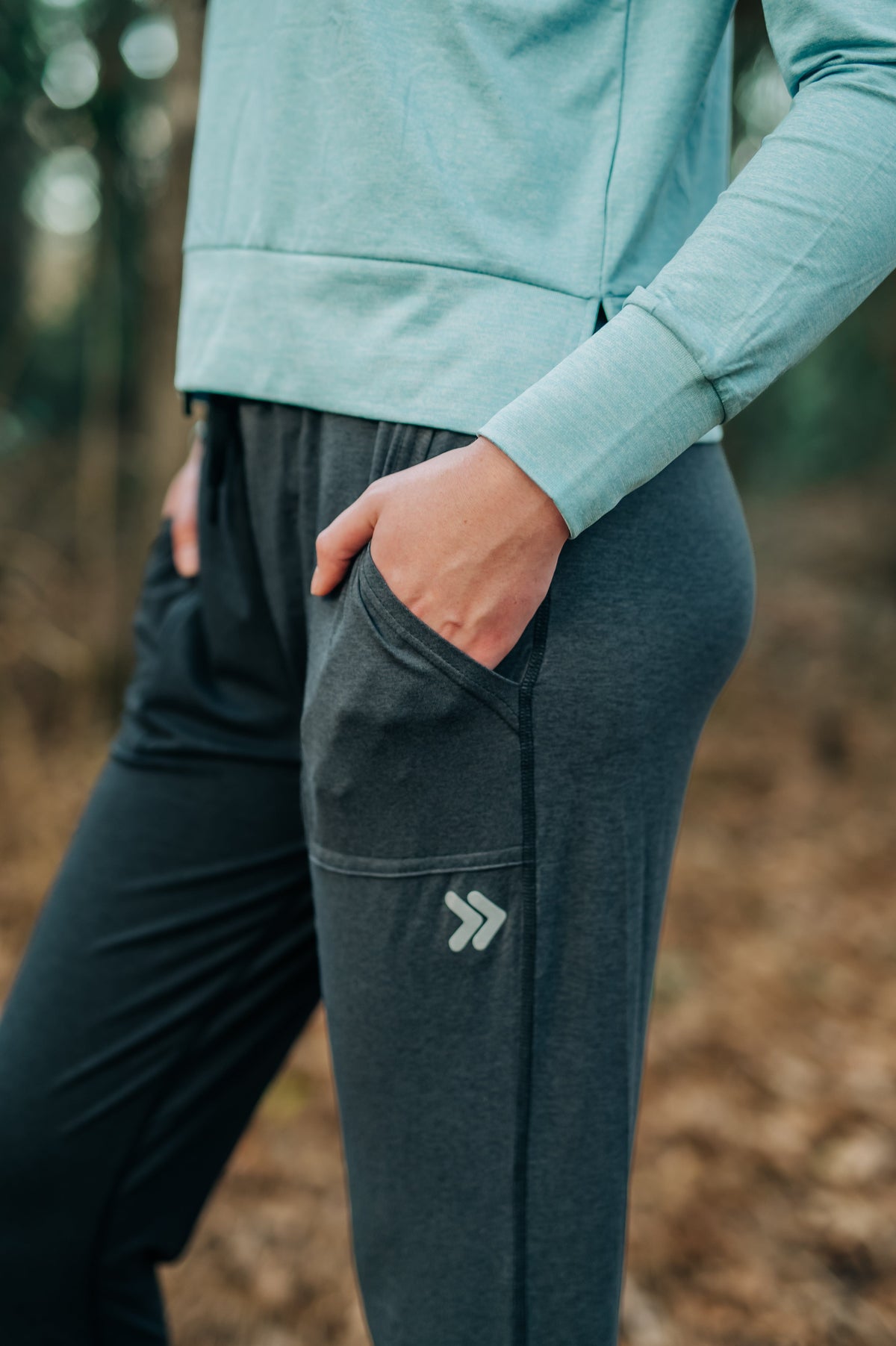 Close-up of a woman wearing dark Essential Joggers outdoors, showing pocket and thigh embellishment.
