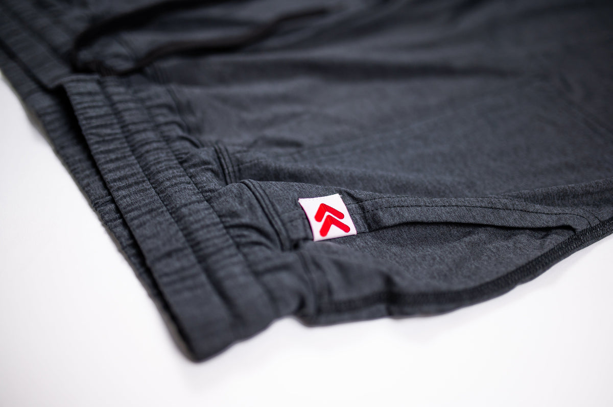 Close-up of fabric stitching and the original red double-chevron tab on black Essential Joggers.
