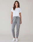 Full-body studio view of a woman wearing grey MOVE Sport Apparel Women’s Essential Joggers with a white tee and trainers, showing the pocket tab and silver reflective thigh embellishment.