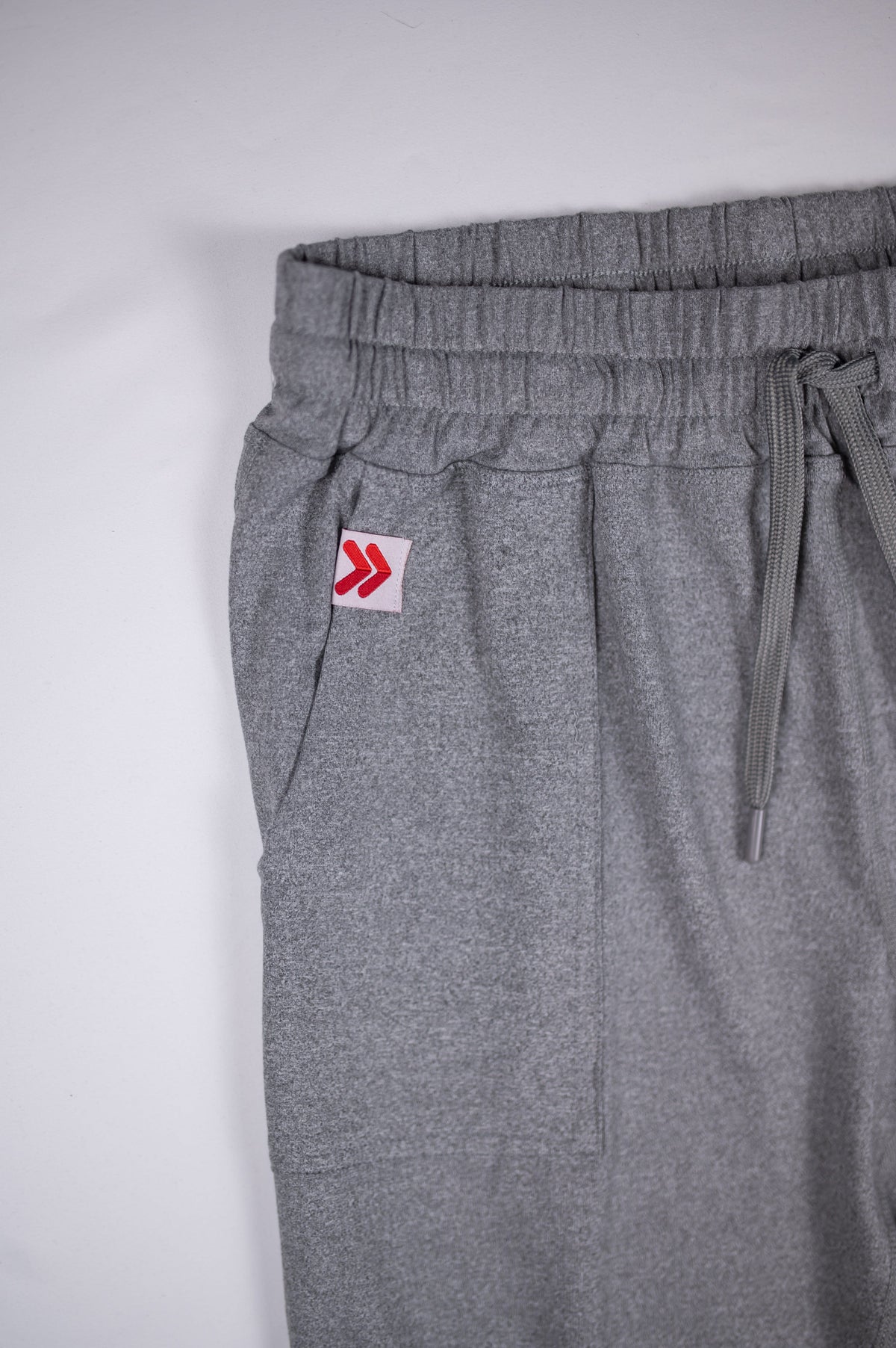 Original white tab with red double chevrons at the grey Essential Joggers pocket opening.