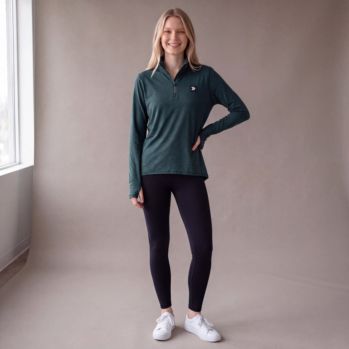Full body studio view of a woman wearing the MOVE Sport Apparel Women’s Essential Quarter Zip in Pine Grove with black leggings.