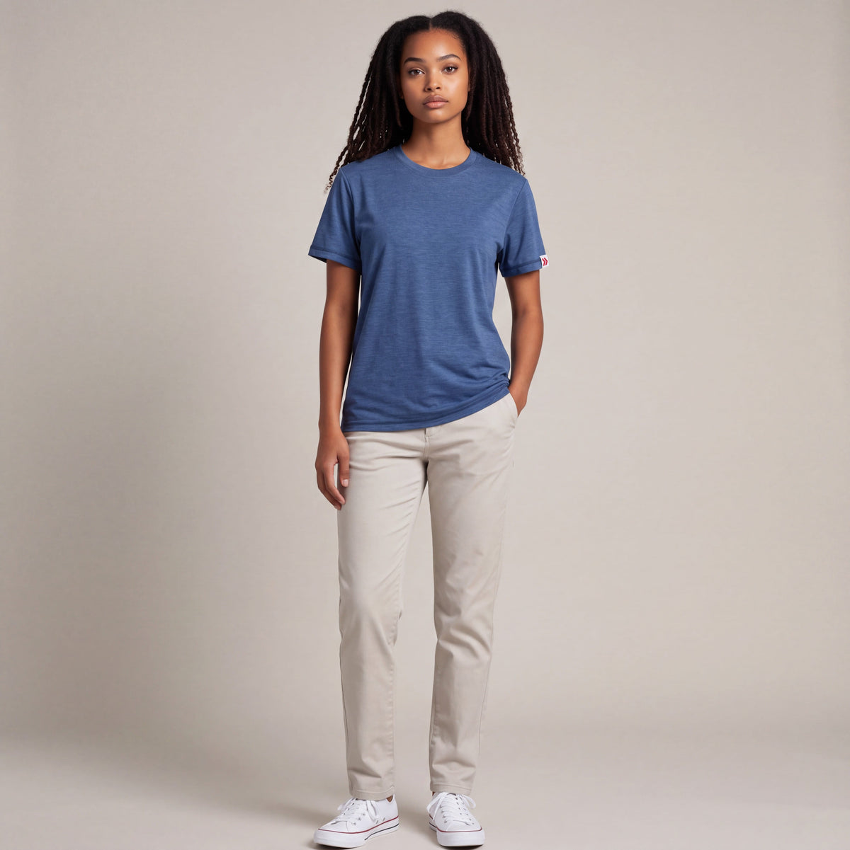 Full-body studio view of a woman wearing the Pageant blue MOVE Sport Apparel women’s Essential Short Sleeve T-shirt with light stone trousers and white trainers.