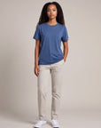 Full-body studio view of a woman wearing the Pageant blue MOVE Sport Apparel women’s Essential Short Sleeve T-shirt with light stone trousers and white trainers.