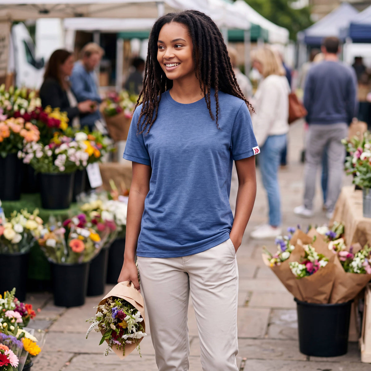 Woman wearing the Pageant blue MOVE Sport Apparel women’s Essential Short Sleeve T-shirt and light stone trousers at an outdoor flower market.