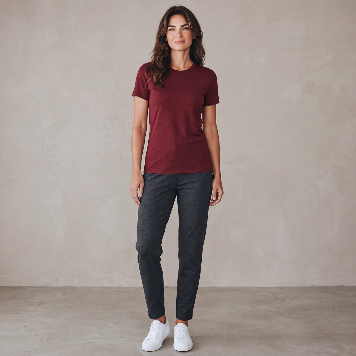 MOVE Sport Apparel women’s Merino Short Sleeve T-Shirt: Full-body studio view of a woman wearing Oxblood Red Merino Short Sleeve T-Shirt with charcoal trousers and white trainers.