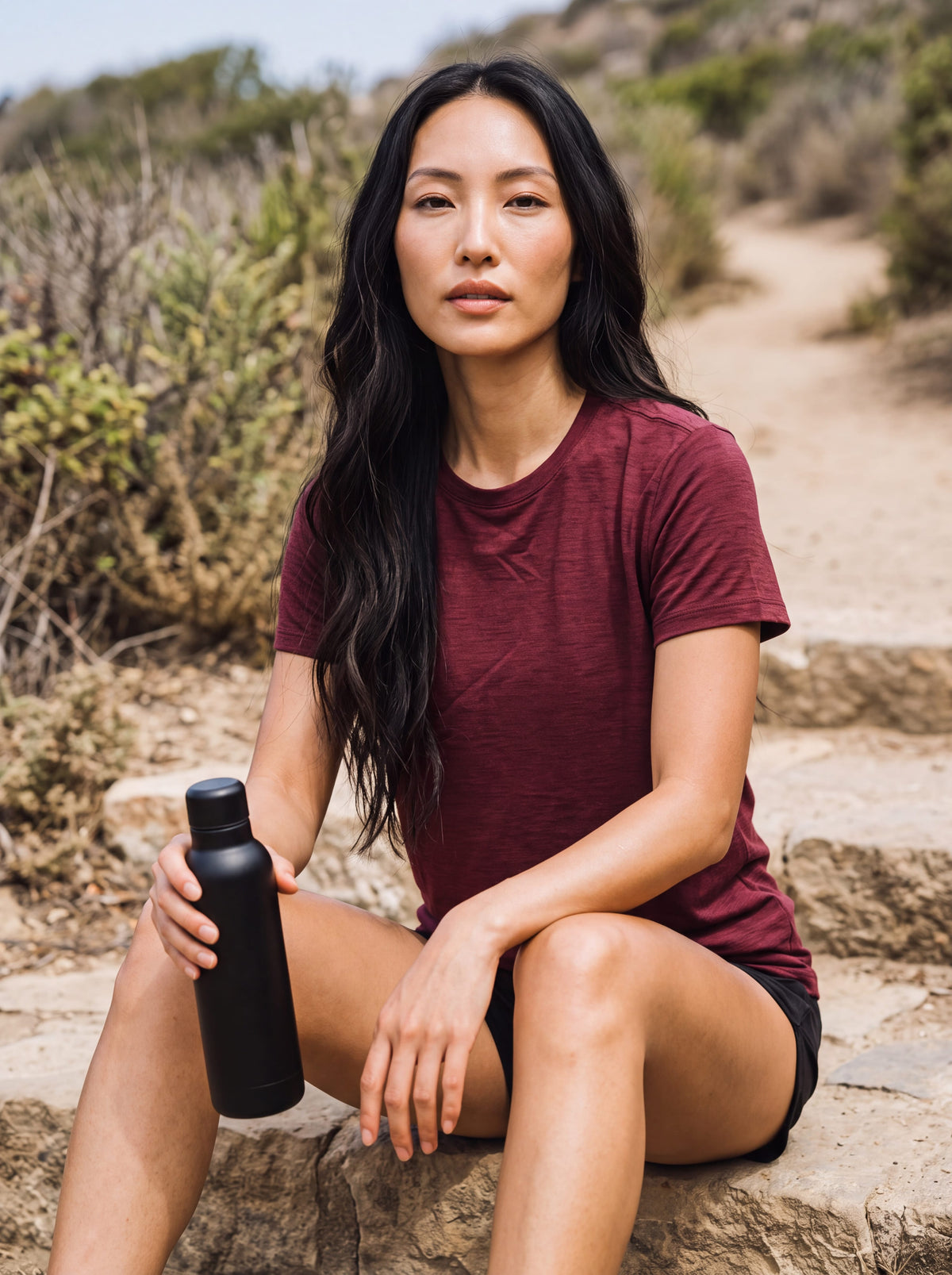 MOVE Sport Apparel women’s Merino Short Sleeve T-Shirt: Woman wearing Oxblood Red Merino Short Sleeve T-Shirt while resting on a stone coastal trail.