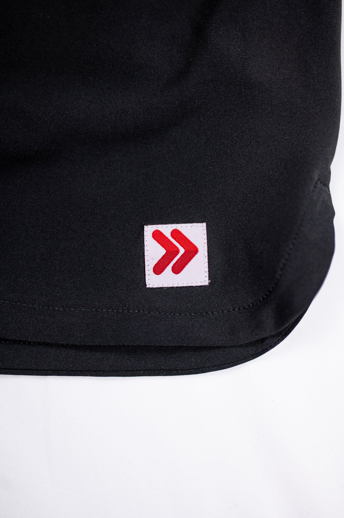 Close-up of the original white square with red double chevrons on the black skort hem.