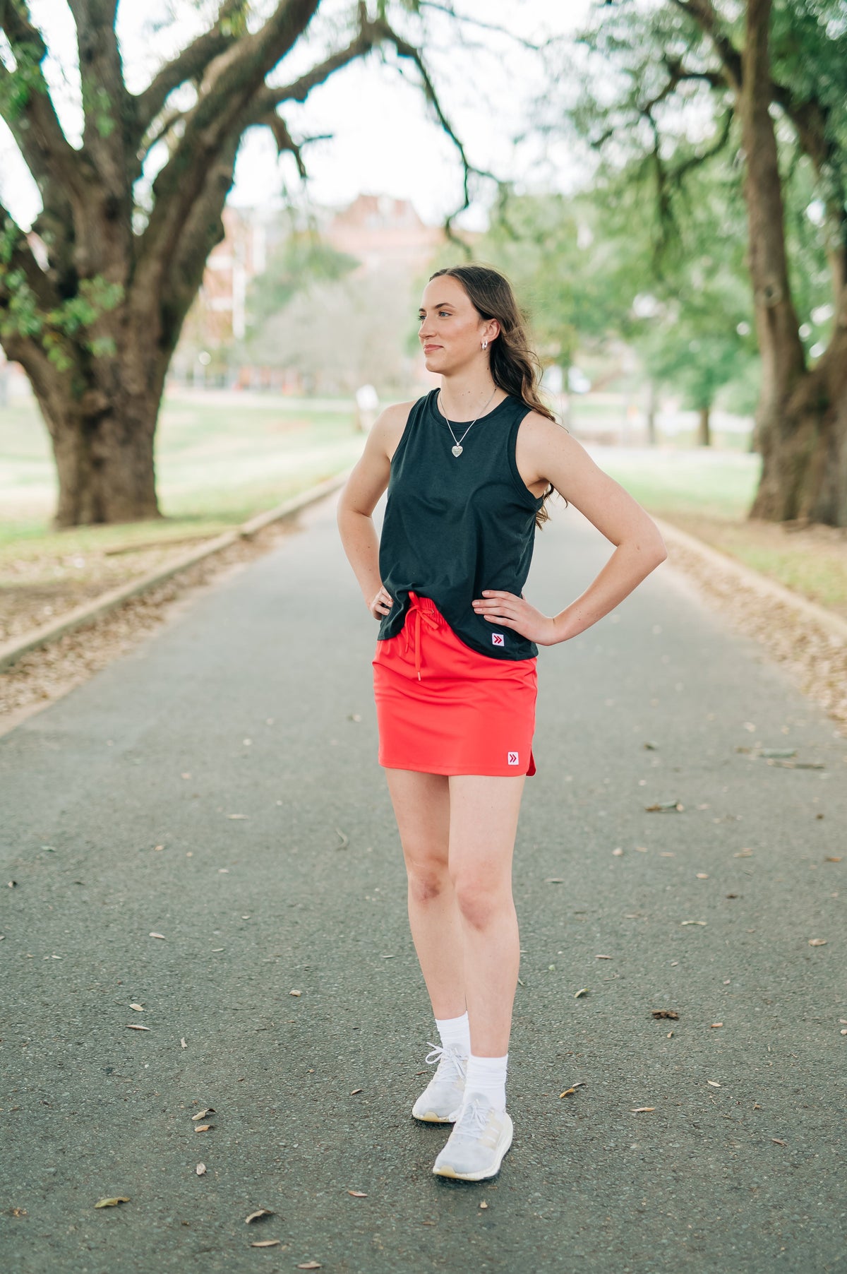 Woman wearing a coral-pink MOVE Sport Apparel women’s Skort with a black sleeveless top on a park path.