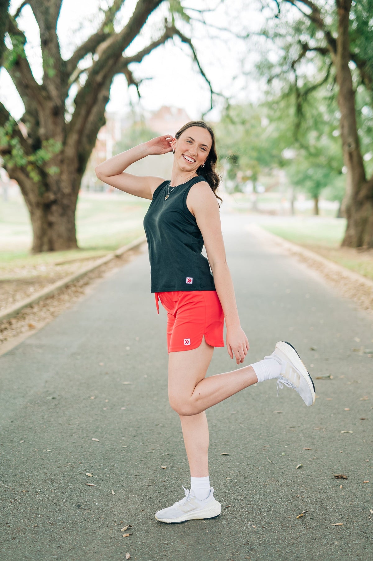 Woman wearing a coral-pink skort during a standing stretch on a tree-lined park path.