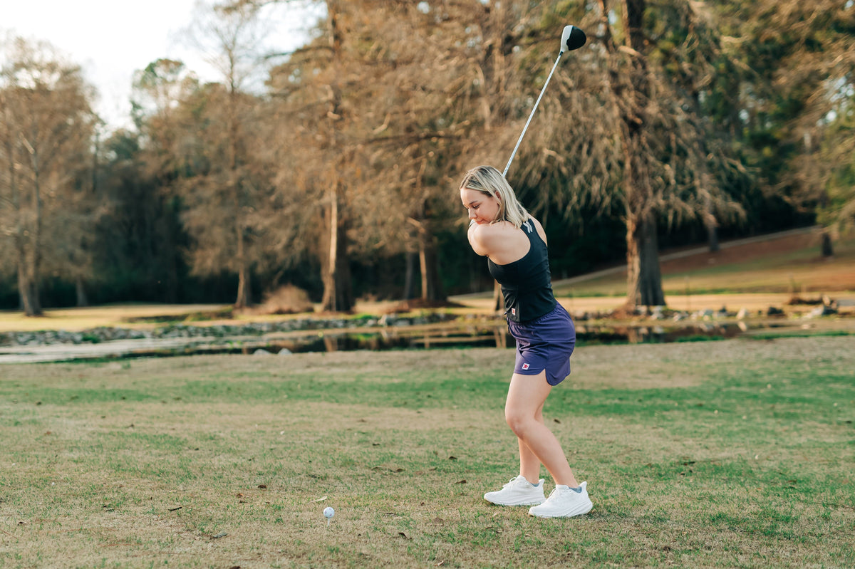 Woman wearing a purple MOVE Sport Apparel women’s Skort while swinging a golf club.