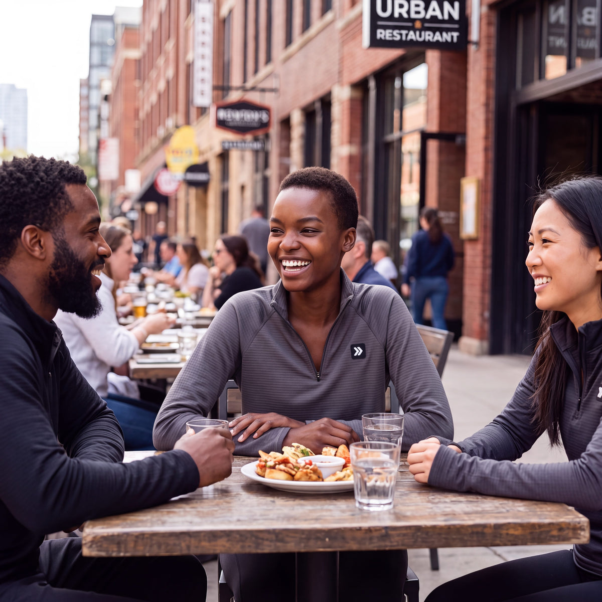 Three friends wearing MOVE sport apparel charcoal grey waffle-knit quarter-zip pullovers laughing at an outdoor cafe.